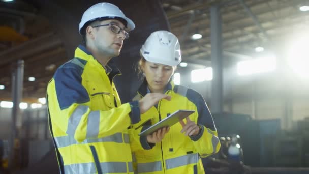 Ingénieurs industriels masculins et féminins dans Hard Hats Discuter nouveau projet tout en utilisant Tablet Computer. Ils prennent des décisions d'ingénierie calculées.Ils travaillent à l'usine de fabrication de l'industrie lourde .