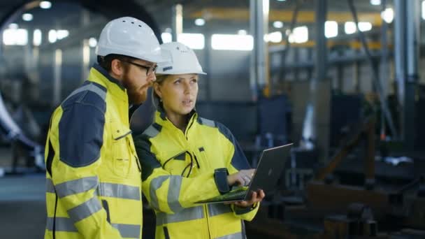 在使用笔记本电脑时 在安全帽中的男性和女性工业工程师讨论新项目 他们表现出手势 他们在重工业制造厂工作 长时间拍摄 — 图库视频影像