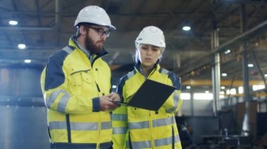 Erkek ve dişi Endüstri mühendisleri ağır sanayi ile fabrika üretim yürürken tartışma ve kullanım Laptop sahip. Sabit şapka ve emanet ceket giymek.