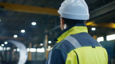 Endüstri Mühendisi Sabit Hat ve emanet ceket büyük ağır fabrika üretim sektöründe etrafına bakıyor. Ark Görünümü görüntüleri.