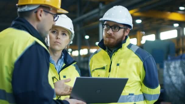 Les ingénieurs industriels masculins et féminins parlent avec le travailleur d'usine tout en utilisant l'ordinateur portable. Ils travaillent à l'usine de fabrication de l'industrie lourde .
