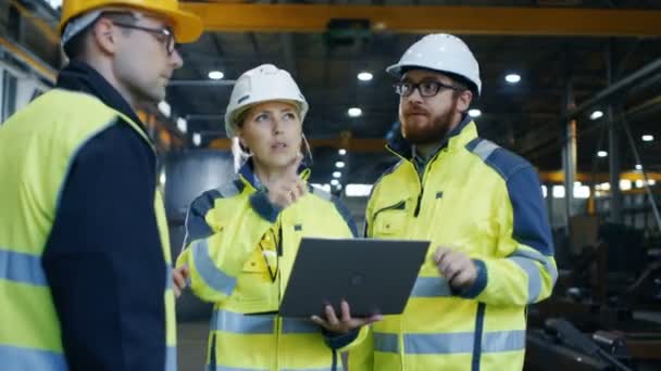 Les ingénieurs industriels masculins et féminins parlent avec le travailleur d'usine tout en utilisant l'ordinateur portable. Ils travaillent à l'usine de fabrication de l'industrie lourde .