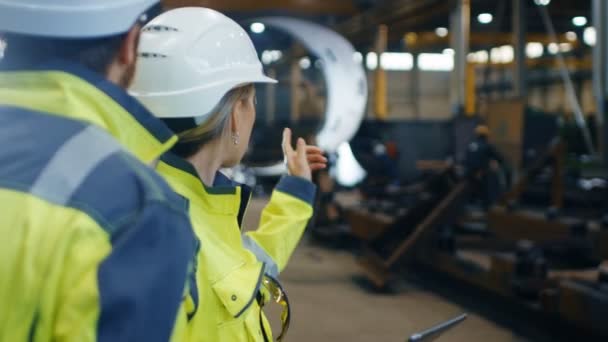 Des ingénieurs industriels masculins et féminins portant des casques durs et des vestes de sécurité discutent d'un nouveau projet lors de l'utilisation d'un ordinateur tablette. Ils travaillent à l'usine de fabrication de l'industrie lourde .
