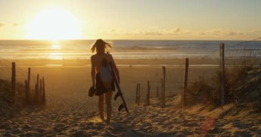 Yan görünümü görüntüleri denize doğru yürüyüş Surfboard taşıma güzel ve genç birbayan. Kız olan sarışın saç ve Backpack.The Beach boş ve güneş batıyor.