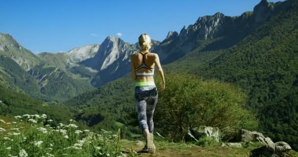 下面的影片的美丽的适合妇女赛跑运动员在运动服慢跑停在小径上休息和欣赏壮丽的山景 迷人的金发女孩和风景优美的自然 在慢动作中长时间拍摄 — 图库视频影像