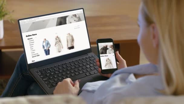 女性を保持しているスマート フォンおよびオンライン参照する彼女の膝の上にノート パソコン ストアその販売のファッショナブルな服 — ストック動画