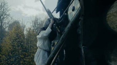 Büyük ölçekli ortaçağ savaş Reenactment. Şiddet kabilesi savaşçıları saldırı tahta kale duvarı, onlar tırmanmaya merdivenler, gardiyanlar deneyin Fortification.They mücadele eksenleri, kılıç, mızrak, ok ve kalkanlar savunmak.