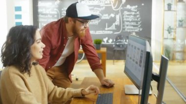 Güzel kadın geliştirici mobil oyun uygulaması tasarlama kişisel bilgisayarında çalışır, Erkek Programer ile konuşuyor. Şık Indie Creative Studio içinde çalışır.