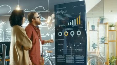 Kadın geliştirici ve erkek istatistikçi kullanım interaktif beyaz tahta sunu Touchscreen çizelgeler, grafikler ve büyüme istatistikleri bakmak için. Şık yaratıcı ofiste çalışmak.