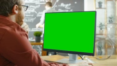 Adam yeşil Mock-up ekran ile kişisel bilgisayar çalışır. Adam çizim kara tahta duvar ile yaratıcı Office arka planda.