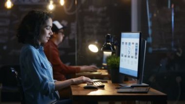 Güzel kadın Mobil Video oyun uygulama geliştiricisi masasının üstünde özel bilgisayar çalışıyor. Arka planda onun meslektaşım yaratıcı ofiste.