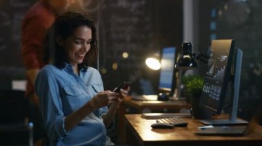Güzel kadın yatırımcı kullandığı cep telefonu, yazılı mesajlar, Smiling.In arka plan yaratıcı ofis çalışanı olan e-postaları.