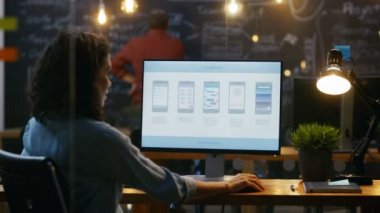 Güzel kadın Mobil Video oyun uygulama geliştiricisi masasının üstünde özel bilgisayar çalışıyor. Arka planda onun meslektaşım yaratıcı ofiste.