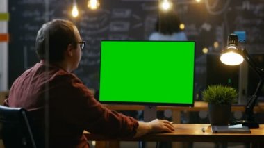 Ofis çalışanı, onun okul sýrasý Mock-up yeşil ekran kişisel bilgisayarda çalışır. Omuz görüntüleri. Meslektaşı arka planda çalışır. Yaratıcı Office akşam.