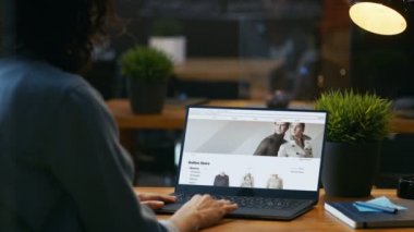Online perakende giyim mağaza web sitesi Laptop bakar ile onun masasında oturan kadın. Site gösterir çeşitli erkek ve kadın şık giysiler, yeni koleksiyon.