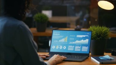 Onun masasında kadın analisti istatistikleri, grafikler ve gösterilen bir dizüstü bilgisayarda çalışır. O yaratıcı ofiste ahşap tabloda çalışıyor.