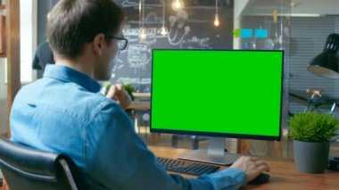 Genç adam inşaat üstünde özel bilgisayar Mock-up ile onun masasında yeşil ekran. Arka planda meslektaşı yaratıcı ofiste çalışıyor..