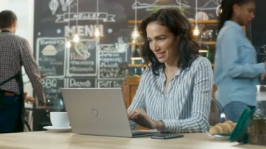 Güzel kadın Cafe otururken bir dizüstü bilgisayarda çalışıyor. Diğer müşteri ve bu şık kahve dükkanı arka planda yürüyen garson.