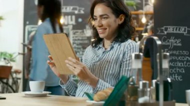 Güzel akıllı kadın kullanır Tablet bilgisayar meşgul Cafe dükkanında otururken. Arka plan şık işyerinde insanlar ve garson.