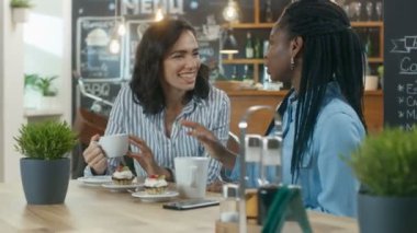 Cafe'de oturan, tatlılar yemek içecekler içme iki güzel kadınlar. Sohbet ve birlikte eğlenmek. Arka plan Modern şık kahve evin içinde.