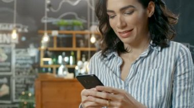Güzel bir kadın oturur kafedeki Smartphone kullanır. Her cep telefonu tarama sırasında gülümsüyor. Arka planda şık Cafe meşgul.