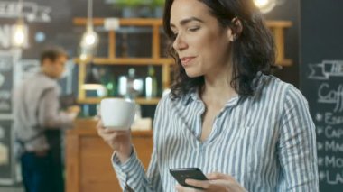 Güzel kadın kullanır Cafe otururken Smartphone. O bardaktan içecek içecekler. Arka plan bu şık Coffee Shop.