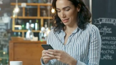 Güzel kadın kullanır Cafe otururken Smartphone. O bardaktan içecek içecekler. Arka plan bu şık Coffee Shop.