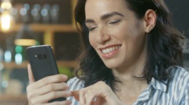 Yakın çekim portre çekim gülümseyen ve cep telefonu kullanarak güzel bir genç kadın. Arka plan şık Cafe.