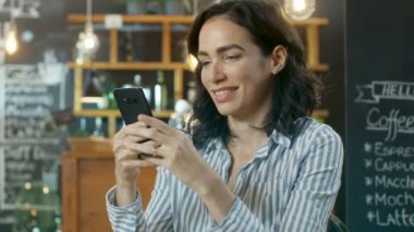 Gülümseyen ve cep telefonu kullanarak güzel bir genç kadının portresi atış. Arka plan şık Cafe.