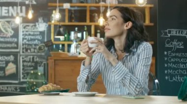 Güzel İspanyol kadın rahatlatır Cafe içinde içki içecek bardaktan görünüyor, Her nerede gelen mesajı Bleeped telefon. Arka plan şık Modern kahve evin içinde.