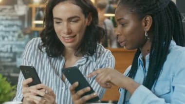 İki güzel kız arkadaşım kafe, onlar göstermek birbirlerine bir şeyler üzerinde onların hareket eden telefon içinde otururken tadını çıkarın. Arka plan şık Modern Cafe.