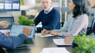 Farklı takım yöneticilerinin bir konferans odasında toplantı var. Paylaştıkları görüşleri, dizüstü ve tablet istatistikler gösteriyor. Şirketin büyüme ilgili uygun bilgilerle arka plan Tv ekranında.