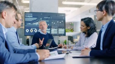 Üst düzey yönetici şirketin vizyon ve potansiyel onun çalışanlara hisse kağıtları açıklar. Onlar konferans odasında büyük masada oturuyorlar. Duvar TV ekranında kurumsal büyüme gösterir.