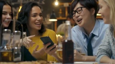 Genç Asyalı adam gösterir ilginç şeyler onlar var iyi zaman ise His Friends için O'nun Smartphone içinde Bar. Gülüyorlar, şaka, şık Hipster Bar işyerinde iç.