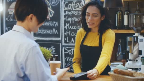 カフェ男は非接触型支払いに携帯電話でコーヒーのテイクアウトを彼の 美しいヒスパニック系の女の子が彼を提供しています — ストック動画
