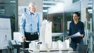 Mimari büro kadın mühendis getiriyor planlar içinde ve kıdemli mimar, onlar tartışmak proje gösterir. Bir yapı modeli kentsel planlamacılar çalışıyorlar.