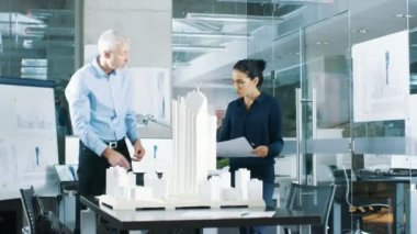 Mimari büro kadın mühendis getiriyor planlar içinde ve kıdemli mimar, onlar tartışmak proje gösterir. Bir yapı modeli kentsel planlamacılar çalışıyorlar.