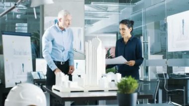 Mimari büro kadın mühendis getiriyor planlar içinde ve kıdemli mimar, onlar tartışmak proje gösterir. Bir yapı modeli kentsel planlamacılar çalışıyorlar.