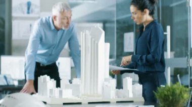 Kadın mühendis planları getiriyor ve kıdemli mimar, onlar tartışmak proje gösterir. Beton duvarları planları ve belgeleri tarafından Bina Model.Clean minimalist Office üzerinde kentsel planlamacılar çalıştıkları.