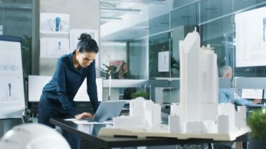 Kadın mimari Tasarımcısı, yeni bina modeli için kentsel tasarım projesi mühendislik bir dizüstü bilgisayarda çalışır. Temiz minimalist Office, beton duvarlar planları ve belgeler.