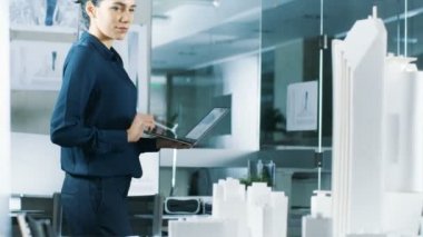 Kadın mimari Tasarımcısı, yeni bina modeli için kentsel tasarım projesi mühendislik bir dizüstü bilgisayarda çalışır. Temiz minimalist Office, beton duvarlar planları ve belgeler.