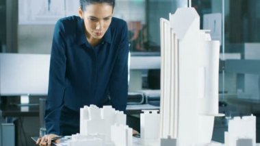 Bir modeli bir şehir ilçe binaları, Parklar ile bir kadın mimari Tasarımcısı çalışır ve kendi ekosistemdir. O gülümsüyor. Temiz minimalist Ofis, planları ve belgeleri tarafından beton duvarları güzel kadın.