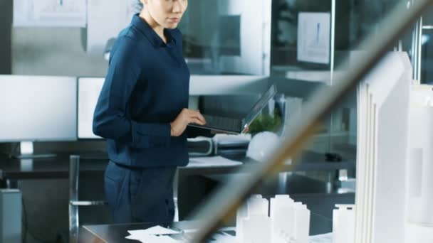 Women Architectural Designer Works on a Laptop, Engineering New Building Model for the Urban Planning Project. Bureau minimaliste propre, murs en béton recouverts de plans directeurs et de documents .
