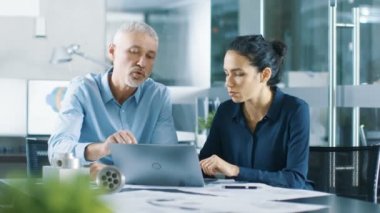 Deneyimli erkek ve kadın Endüstri mühendisleri tartışmak devam eden proje, bir dizüstü bilgisayarda çalışırken. Onlar makine bileşen tasarımı.