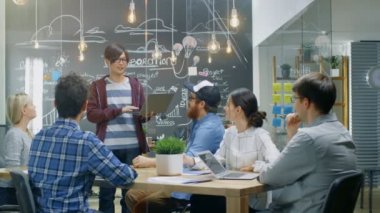 Karizmatik Asya takım lideri Laptop yetenekli genç geliştiriciler farklı bir grup için gösterir, tartışma toplantı masasında başlarlar. Şık ofis ortamında yaratıcı insanlar.