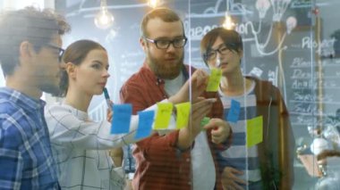 Genç geliştiriciler farklı takım beyin fırtınası, tartışma ve kullanım cam kurulu ve yapışkan kağıtları yeni planları Conceptualize için ellerinde. Şık ofis ortamında yaratıcı insanlar.