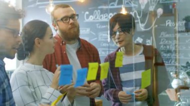 Genç geliştiriciler farklı takım beyin fırtınası, tartışma ve kullanım cam kurulu ve yapışkan kağıtları yeni planları Conceptualize için ellerinde. Şık ofis ortamında yaratıcı insanlar.