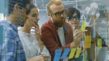 Genç geliştiriciler farklı takım beyin fırtınası, tartışma ve kullanım cam kurulu ve yapışkan kağıtları yeni planları Conceptualize için ellerinde. Şık ofis ortamında yaratıcı insanlar.