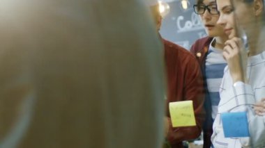 Genç geliştiriciler farklı takım beyin fırtınası, tartışma ve kullanım cam kurulu ve yapışkan kağıtları yeni planları Conceptualize için ellerinde. Şık ofis ortamında yaratıcı insanlar.