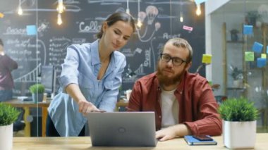 Kadın tasarımcılar görüşmeler erkek geliştirici hakkında devam eden proje o inşaat üstünde a Laptop süre. Arka planda şık genç moda ofis ortamında insanlar..